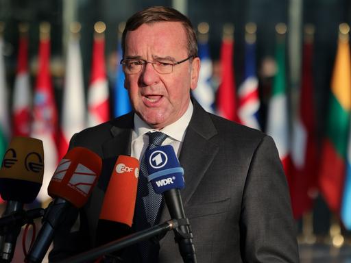 Brüssel: Boris Pistorius, Bundesverteidigungsminister, spricht im Nato-Hauptquartier zu Reportern. Vor ihm Mikrofone, hinter ihm verschwommen die Flaggen der NATO-Länder.