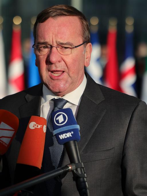 Brüssel: Boris Pistorius, Bundesverteidigungsminister, spricht im Nato-Hauptquartier zu Reportern. Vor ihm Mikrofone, hinter ihm verschwommen die Flaggen der NATO-Länder.
