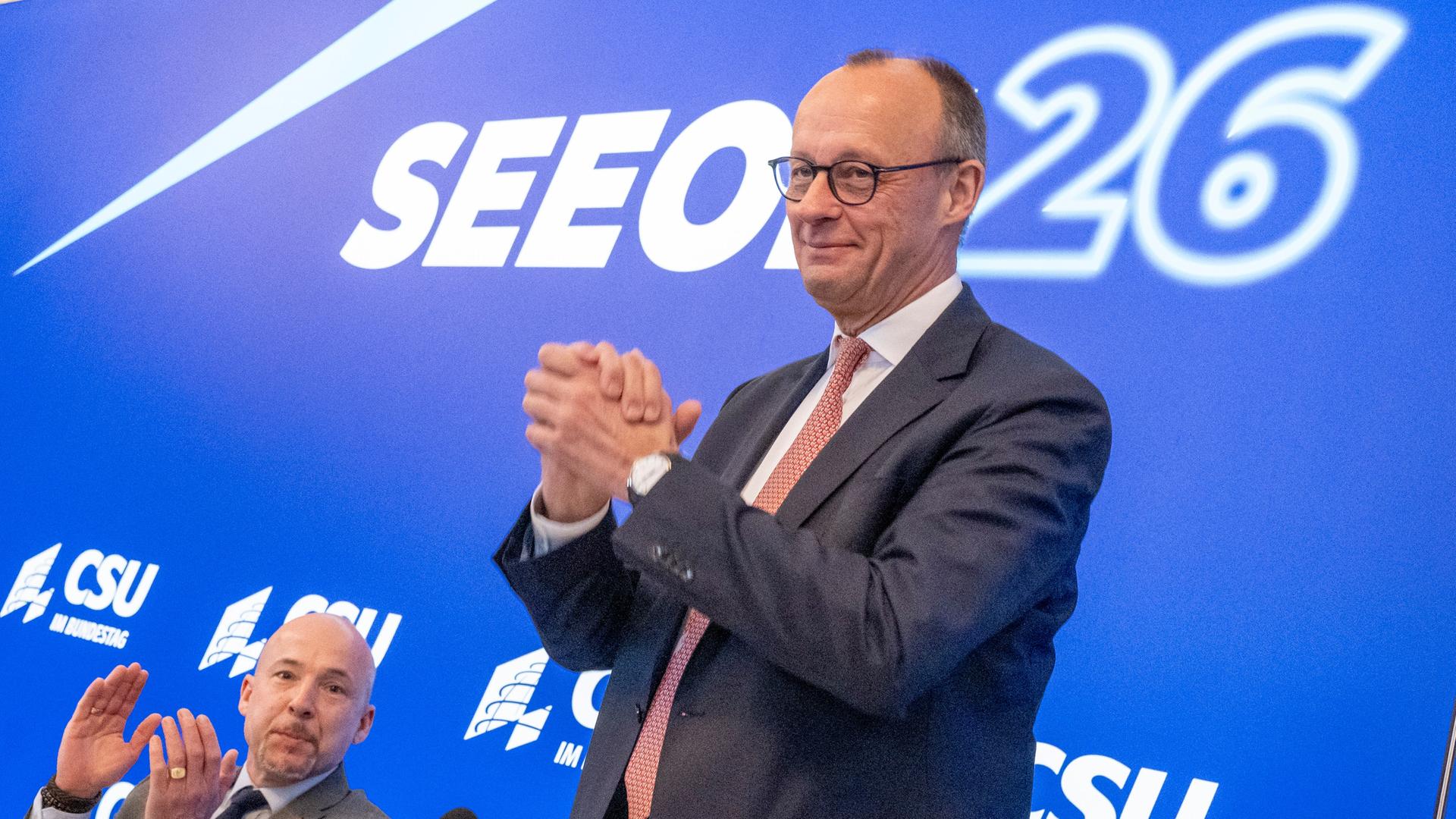 Zu sehen sind Alexander Hoffmann und Bundeskanzler Friedrich Merz. Im Hintergrund zu sehen ist eine blaue Wand mit dem Schriftzug "Seeon 26".
