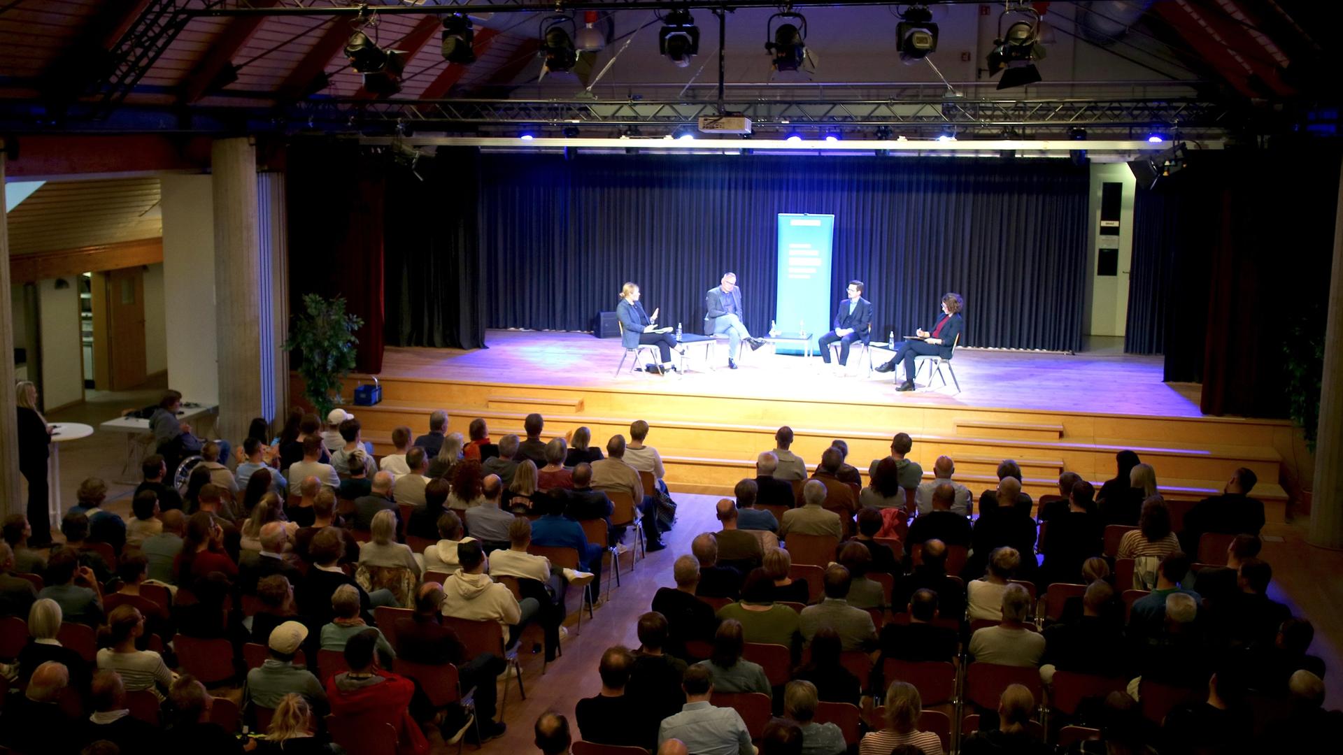 Im Kulturzentrum der Samtgemeinde Meinersen lauscht ein Publikum der Aufzeichnung eines Livepodcasts auf einer Bühne