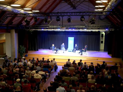 Im Kulturzentrum der Samtgemeinde Meinersen lauscht ein Publikum der Aufzeichnung eines Livepodcasts auf einer Bühne