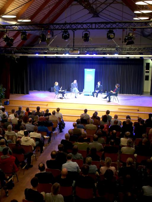 Im Kulturzentrum der Samtgemeinde Meinersen lauscht ein Publikum der Aufzeichnung eines Livepodcasts auf einer Bühne