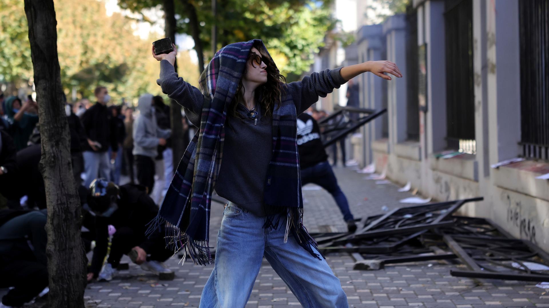 Albanien, Tirana: Eine vermummte Demonstrantin wirft während der Zusammenstöße einen Stein in Richtung des Bildungsministeriums.