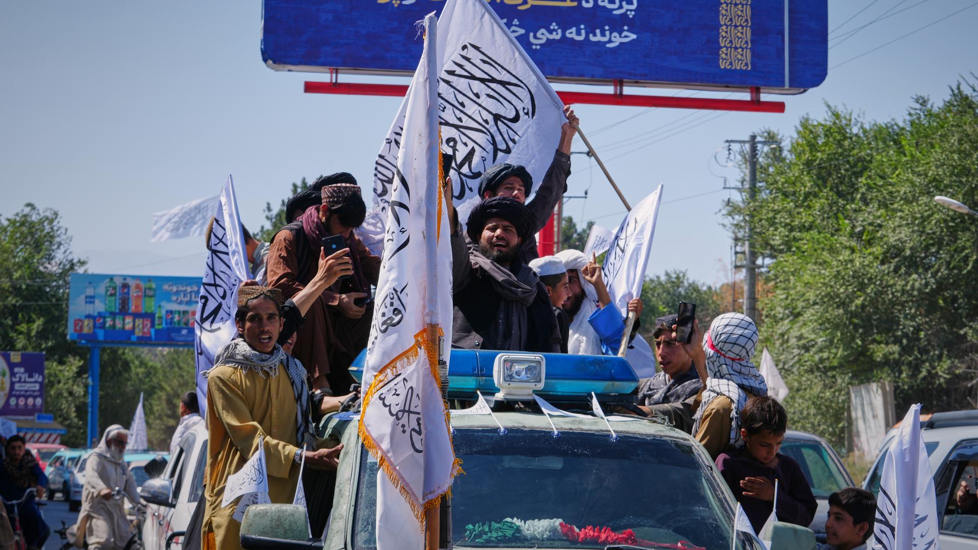 Anhänger der Taliban-Regierung fahren auf einem Auto mit und schwenken Fahnen.