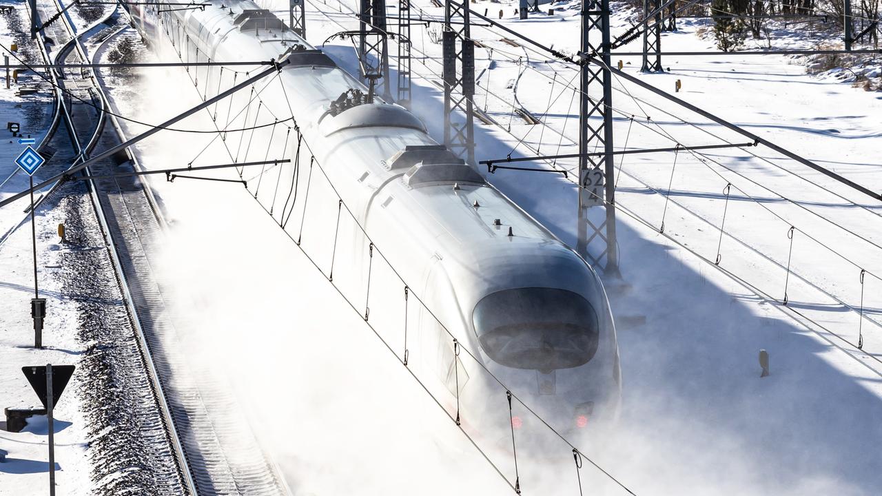 Ein ICE Zug fährt in einer Schneewolke und ist vor dem weiß des Schnees nur schemenhaft zu erkennen.