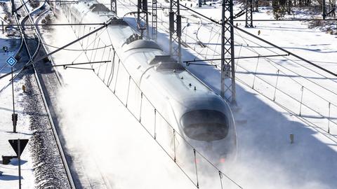 Ein ICE Zug fährt in einer Schneewolke und ist vor dem weiß des Schnees nur schemenhaft zu erkennen.