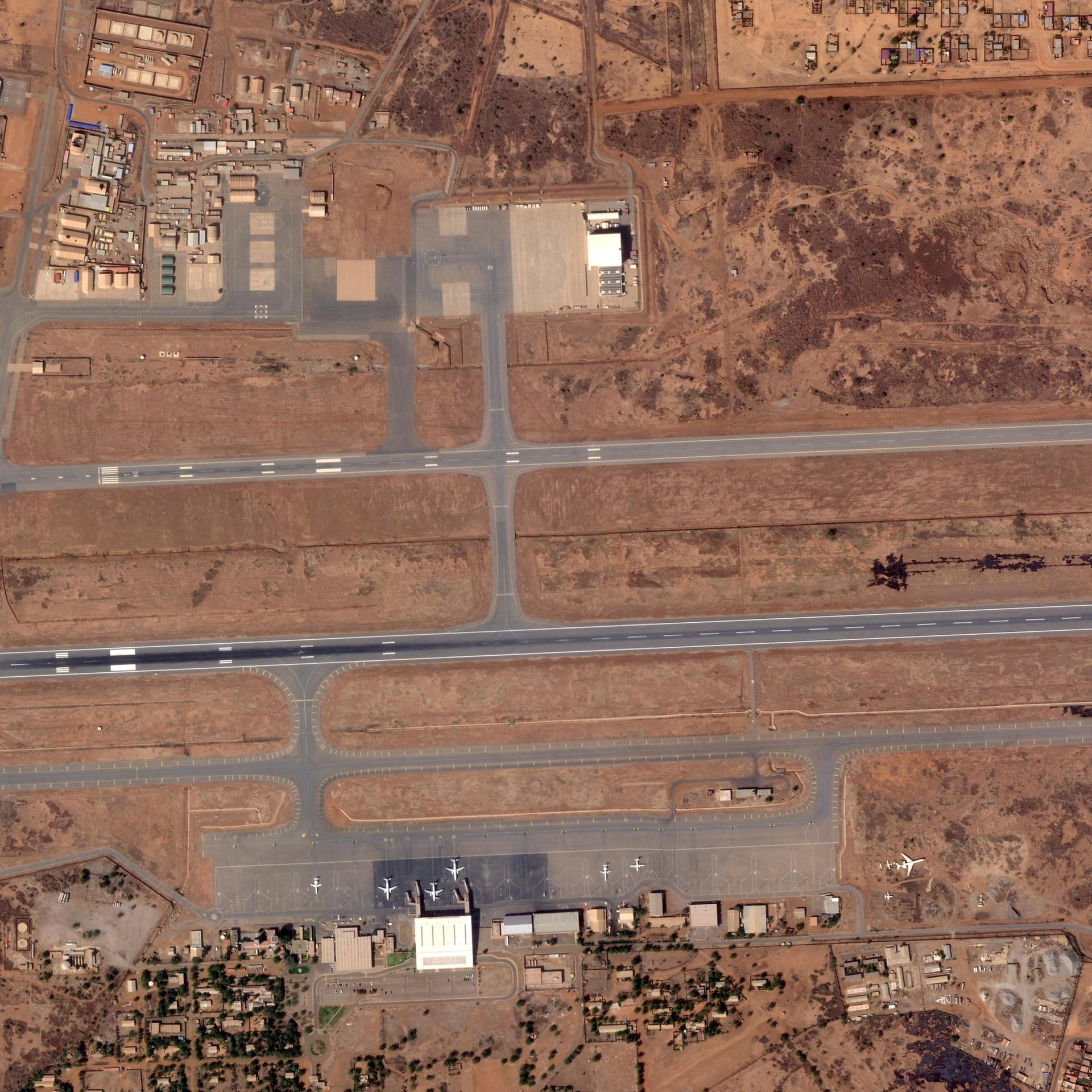 Die Aufnahme aus der Luft zeigt Start- und Landebahnen in einer rötlichen Landschaft. Danben stehe mehrere Flughafengebäude.