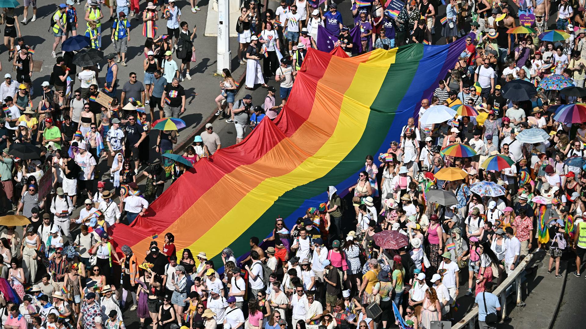 Teilnehmer der Pride Parade in Budapest tragen eine große Regenfahne durch die Menge. 