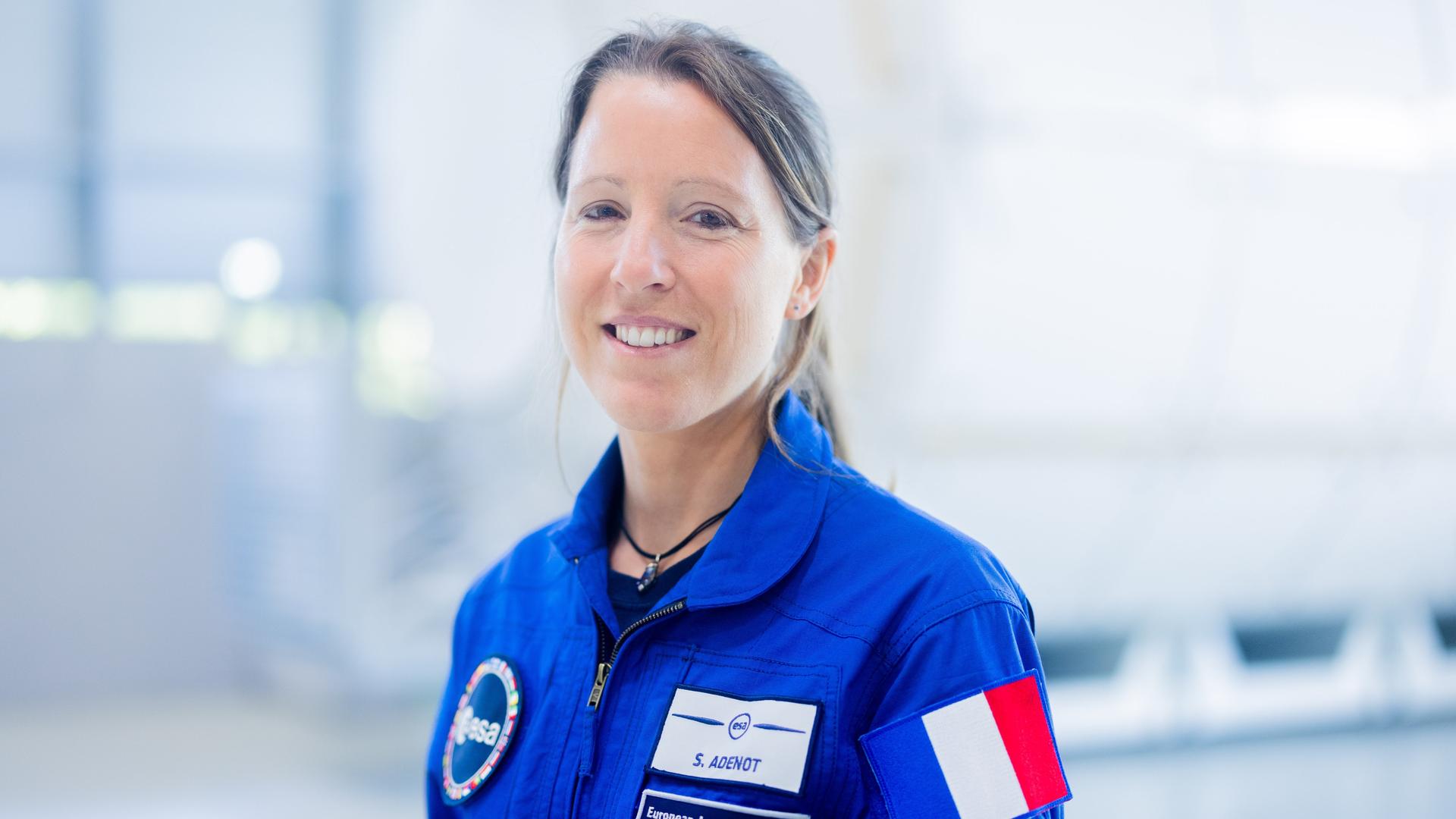 Sophie Adenot aus Frankreich lächelt in die Kamera. Sie trägt einen blauen Anzug der ESA.
