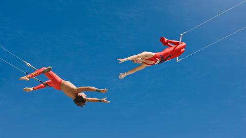 Zwei Trapezkünstler vor blauem Himmel. Sie strecken sich die Arme gegenseitig zu. Zwei Trapezkünstler vor blauem Himmel. Sie strecken sich die Arme gegenseitig zu.