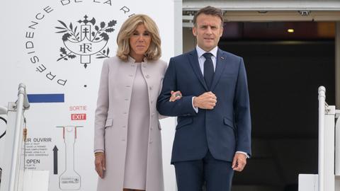 Frankreichs Präsident Macron steht gemeinsam mit seiner Frau vor der Tür eines Flugzeugs.