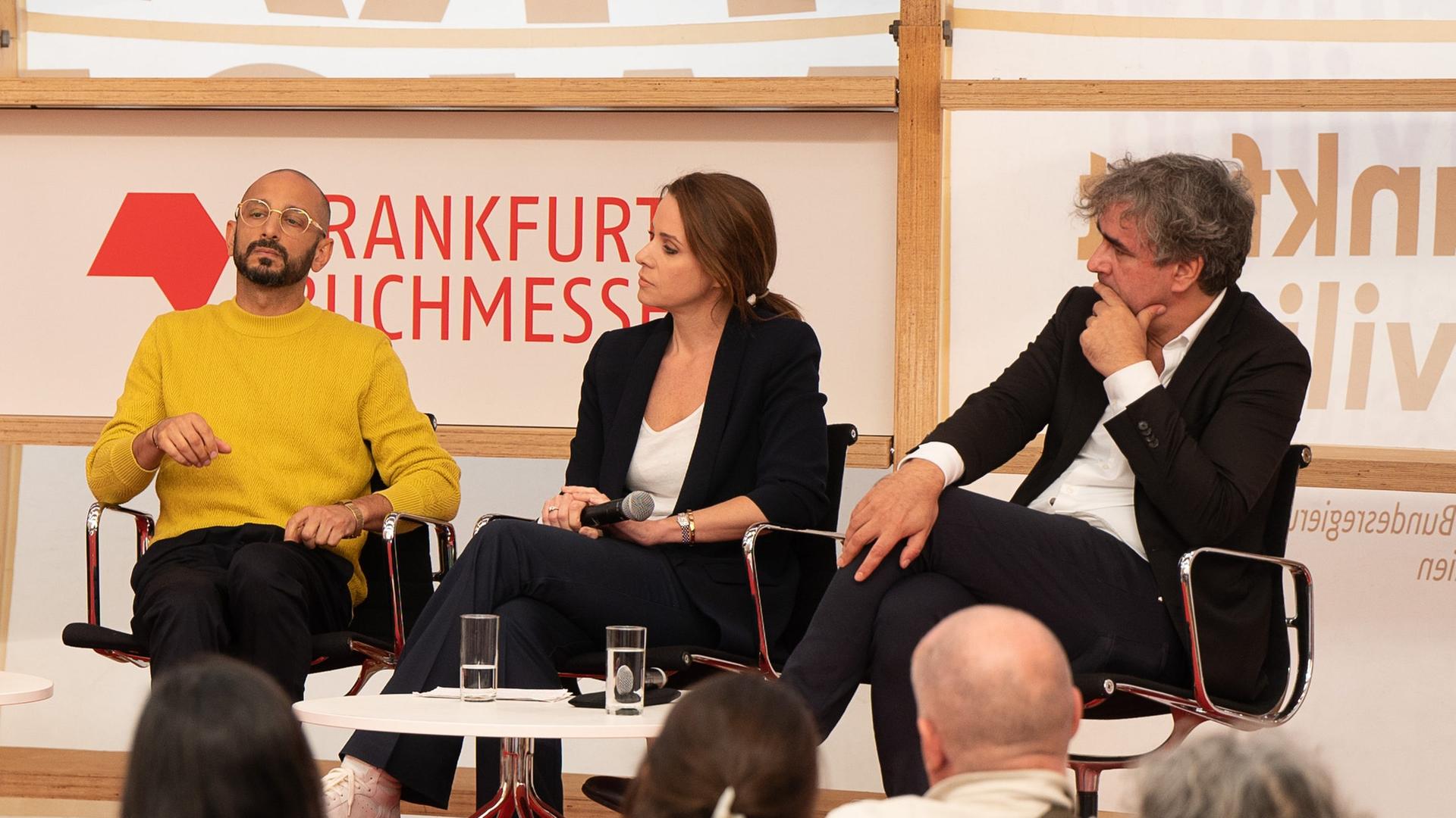 Der Schriftsteller Behzad Karim Khani, die Fernsehmoderatorin Natalie Amiri und der Journalisten Deniz Yücel sitzen auf Stühlen bei einer Diskussionsrunde auf der Frankfurter Buchmesse. Der Schriftsteller Behzad Karim Khani, die Fernsehmoderatorin Natalie Amiri und der Journalisten Deniz Yücel sitzen auf Stühlen bei einer Diskussionsrunde auf der Frankfurter Buchmesse.