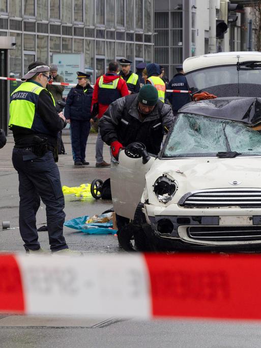 Polizisten stehen um das verbeulte Auto herum, mit dem ein Mann in München in eine Menschengruppe gefahren war.