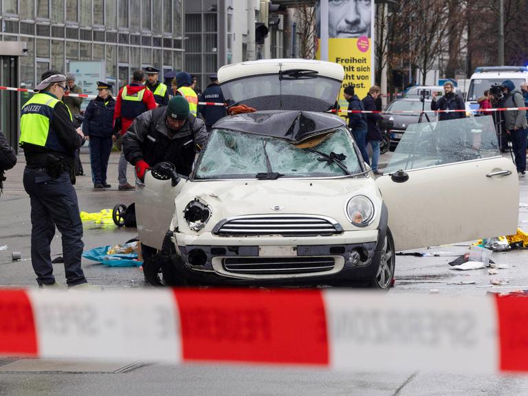 Polizisten stehen um das verbeulte Auto herum, mit dem ein Mann in München in eine Menschengruppe gefahren war.