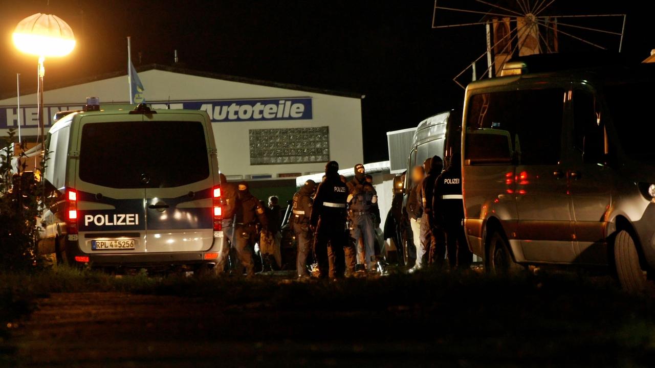 Ein Einsatzwagen der Polizei steht vor einer Halle, daneben mehrere Polizisten in Uniform. Ein Einsatzwagen der Polizei steht vor einer Halle, daneben mehrere Polizisten in Uniform.