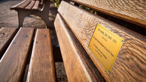 An der Lehne einer Parkbank ist ein kleines Messingschild mit einer Widmung angebracht.