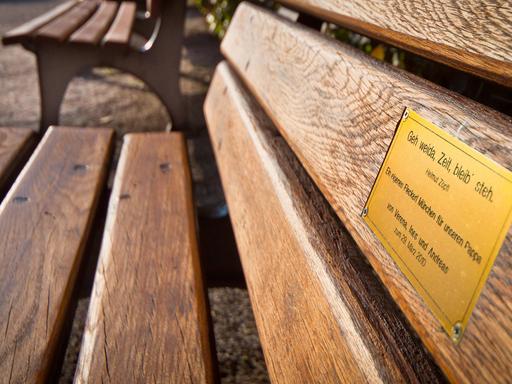 An der Lehne einer Parkbank ist ein kleines Messingschild mit einer Widmung angebracht.