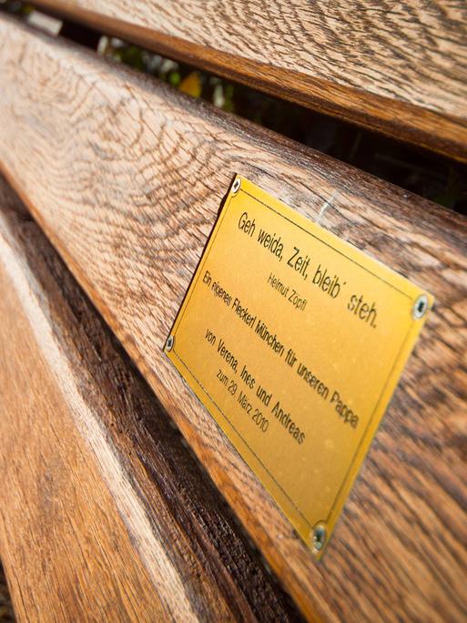 An der Lehne einer Parkbank ist ein kleines Messingschild mit einer Widmung angebracht.