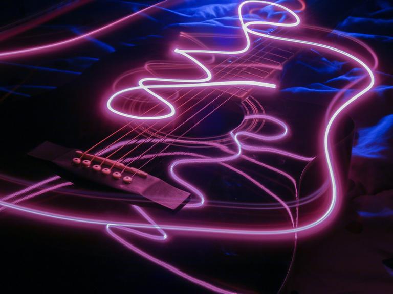 Blick auf eine Gitarre, die virtuell von lilafarbenen Lichtern durchbrochen wird.
