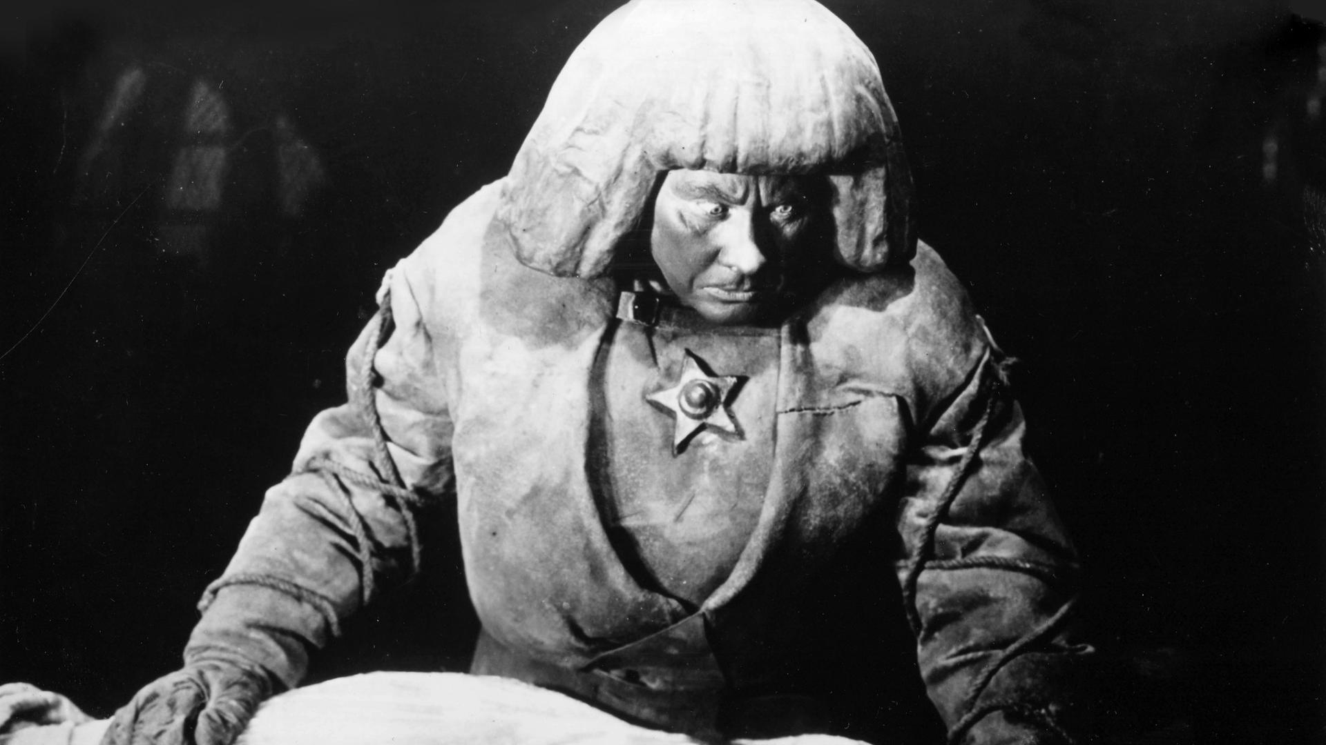 Filmszene aus "Der Golem, wie er in die Welt kam" von 1920. Darin zu sehen ist Paul Wegener als Golem, wie er sich über eine liegende Frau beugt.