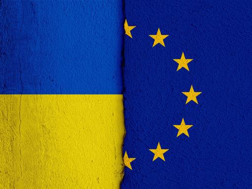 [M] Die Nationalflagge der Ukraine und die Flagge der Europäischen Union auf einer Wand mit einem vertikalen Absatz bzw. Riss in der Mitte und zwei unterschiedlichen Putzarten. Foto mit Composing als Symbolbild für das Verhältnis zwischen der Ukraine und der EU.