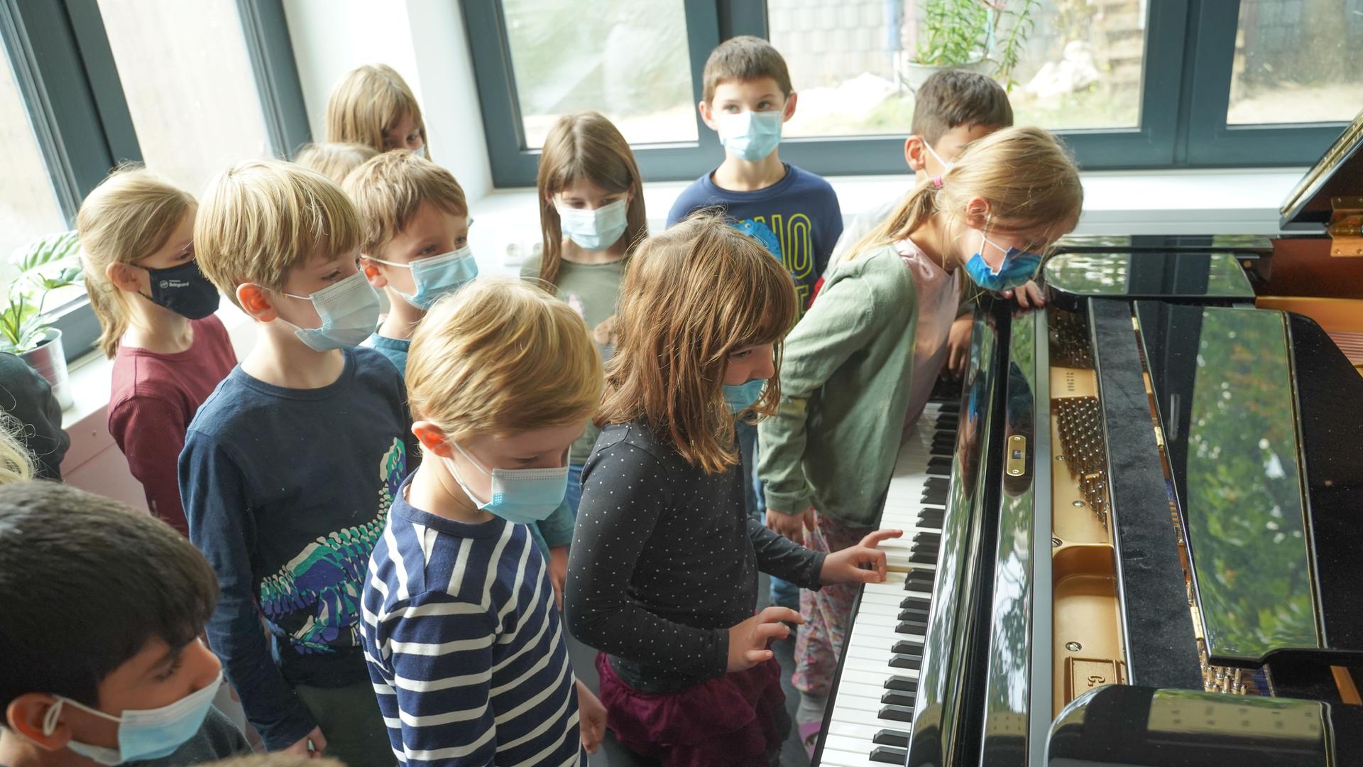 Schüler einer Grundschule stehen mit Masken an einem Flügel Schüler einer Grundschule stehen mit Masken an einem Flügel