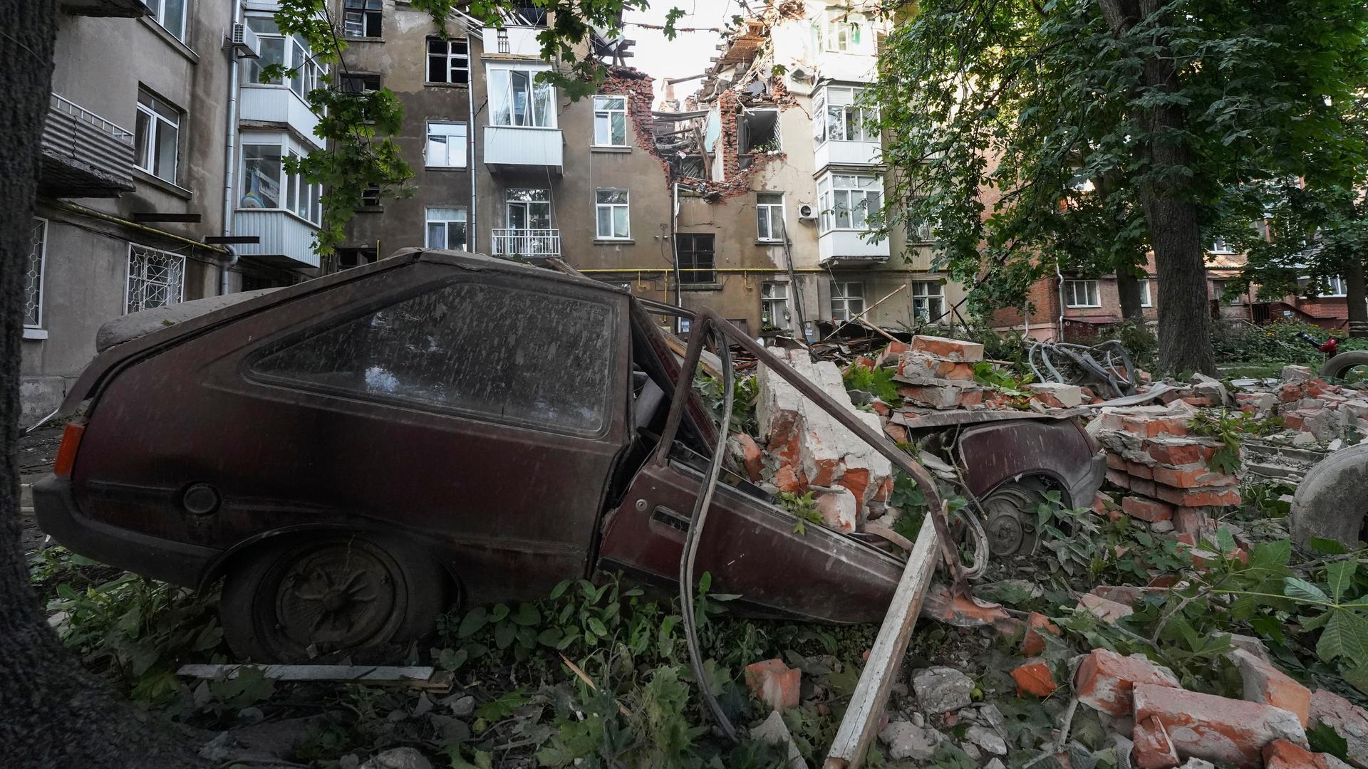 Ukraine, Sumy: Ein Autowrack ist nach einem Angriff vor einem beschädigten Wohnhaus zu sehen.