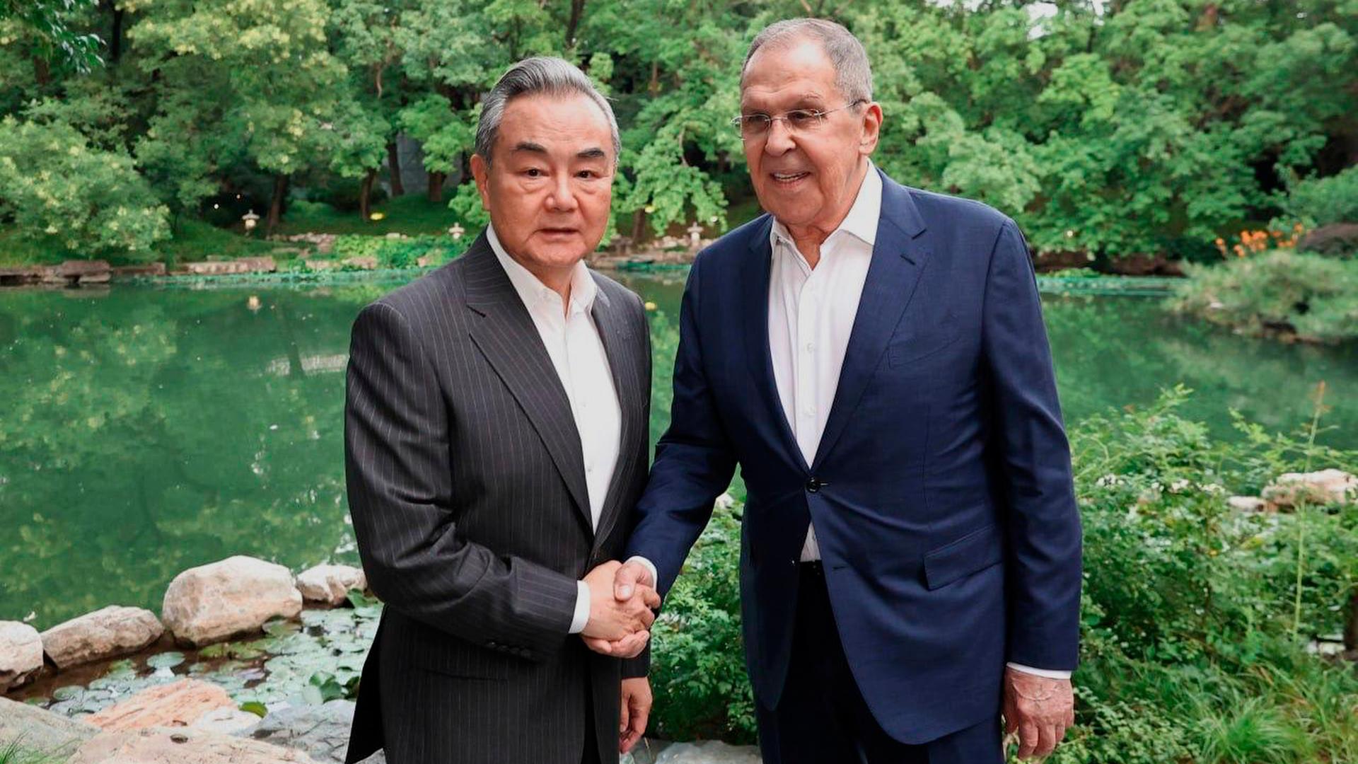Auf diesem vom Pressedienst des russischen Außenministeriums via AP veröffentlichten Fotos geben sich der russische Außenminister Sergej Lawrow (re.) und Chinas Außenminister Wang Yi die Hand. Im Hintergrund ist ein Garten mit Teich zu sehen. 