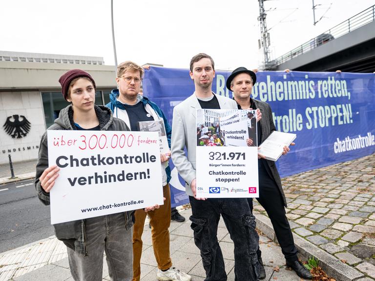 Mitglieder des Bündnis «Chatkontrolle Stoppen!» demonstrieren vor dem Bundesinnenministerium und präsentieren gesammelte Unterschriften. Sie halten Schilder vor sich.