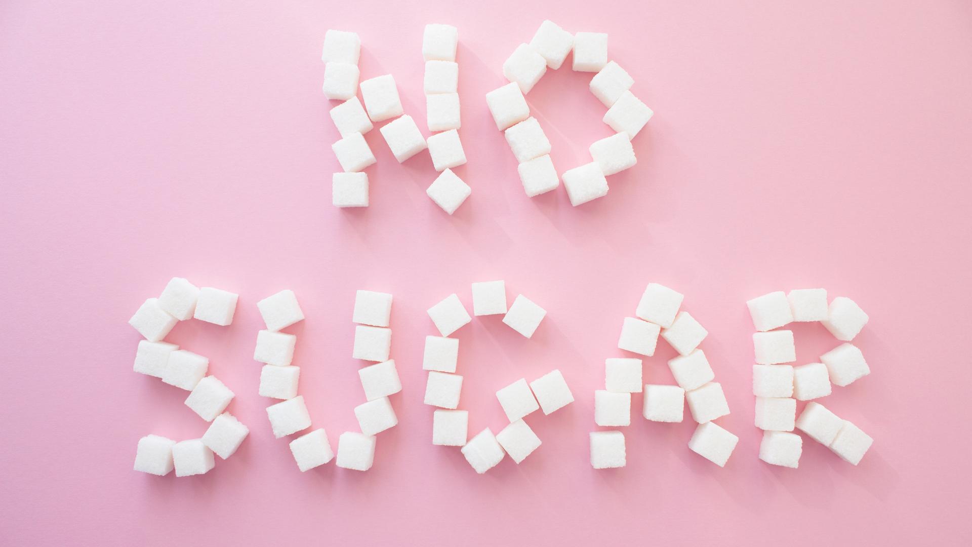 Mehrere Zuckerwürfel bilden auf einem rosafarbenen Hintergrund dern Schriftzug "No Sugar". Mehrere Zuckerwürfel bilden auf einem rosafarbenen Hintergrund dern Schriftzug "No Sugar".