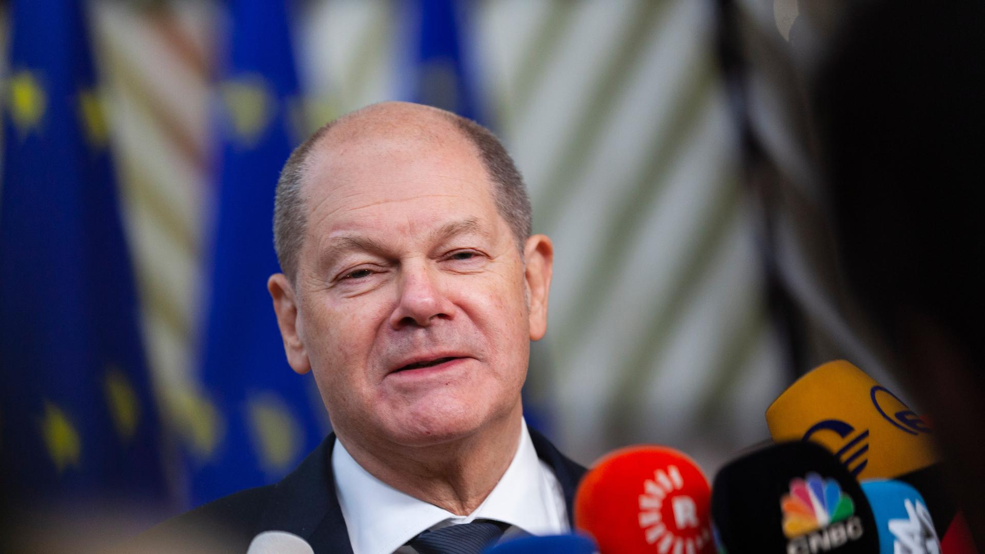 Bundeskanzler Olaf Scholz steht vor EU-Flaggen und spricht in Mikrofone