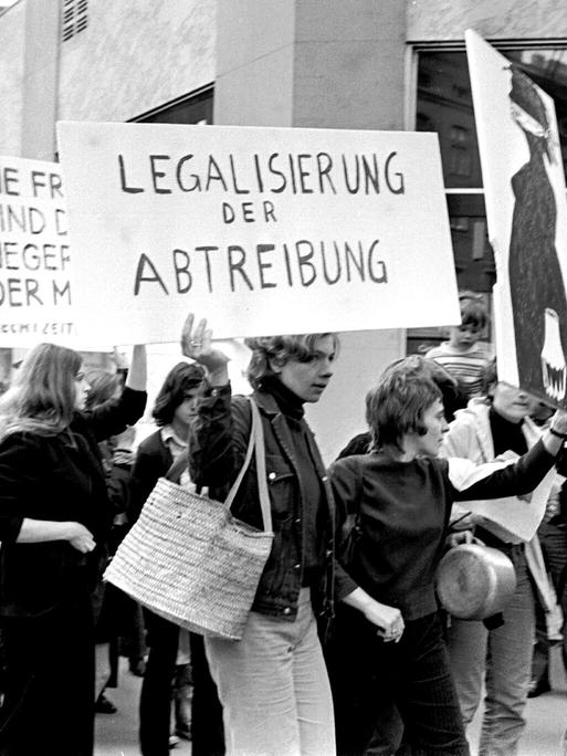 Historisches Schwarzweißfoto demonstrierender Frauen, von der eine ein Schild trägt mit der Aufschrift: "Legalisierung der Abtreibung".