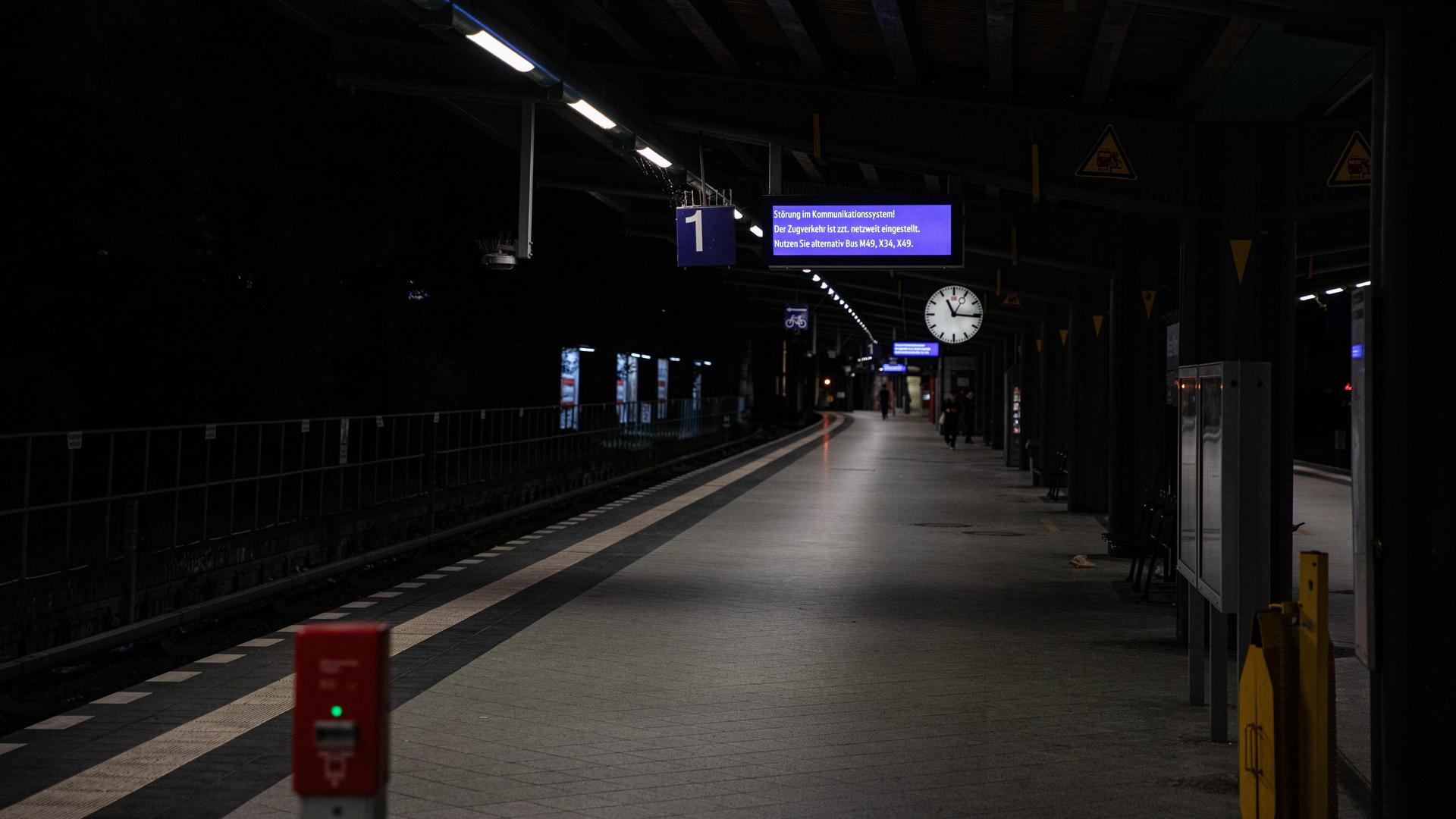 Ein Mensch läuft nachts weit hinten auf einem leeren Bahn-Steig. Oben hängt eine Uhr.