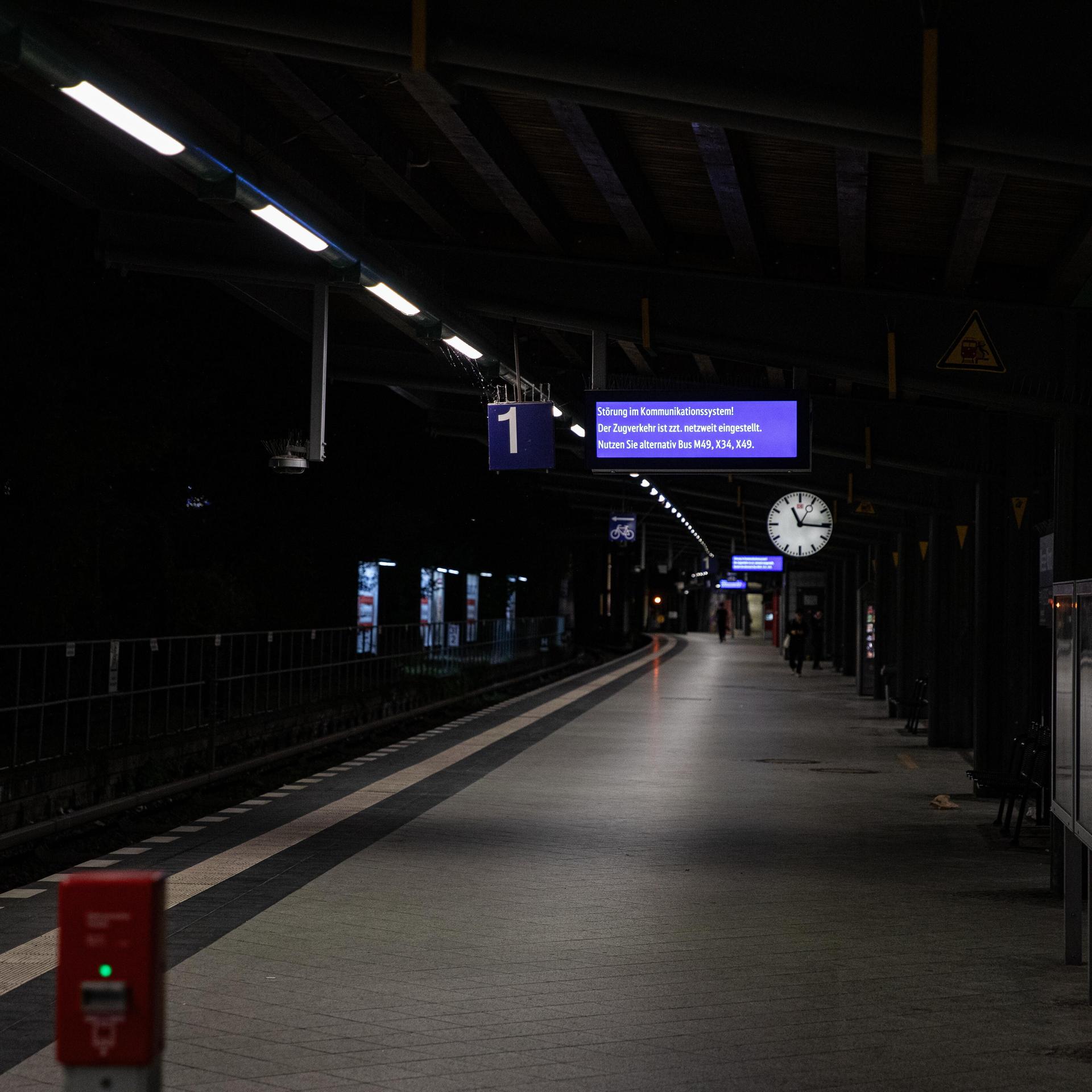 Ein Mensch läuft nachts weit hinten auf einem leeren Bahn-Steig. Oben hängt eine Uhr.