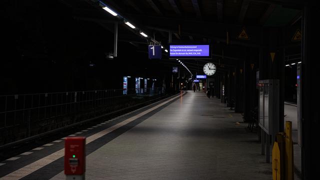 Ein Mensch läuft nachts weit hinten auf einem leeren Bahn-Steig. Oben hängt eine Uhr.