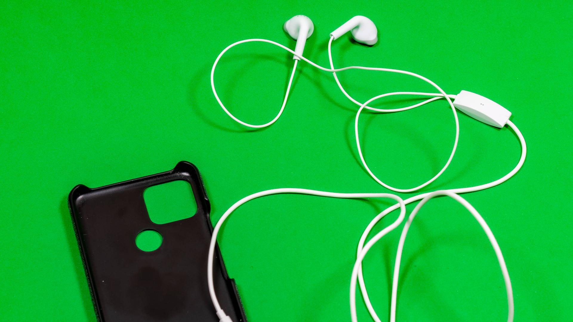 Eine Handytasche mit Kopfhörern liegt auf einer grünen Oberfläche