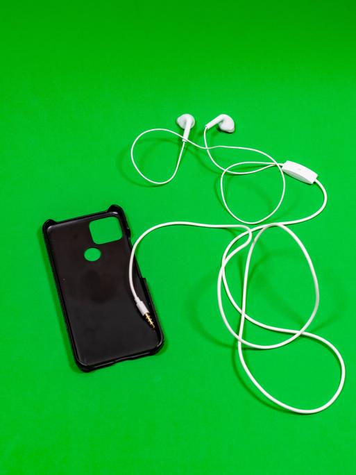 Eine Handytasche mit Kopfhörern liegt auf einer grünen Oberfläche