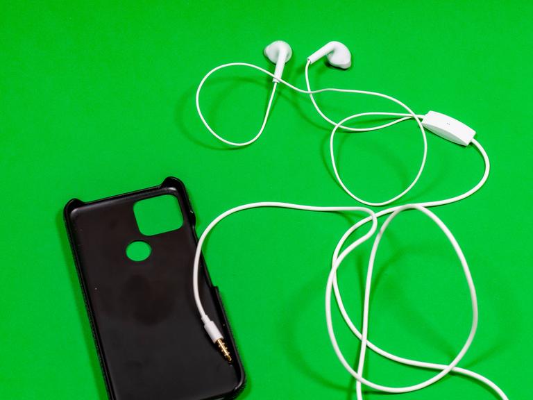Eine Handytasche mit Kopfhörern liegt auf einer grünen Oberfläche