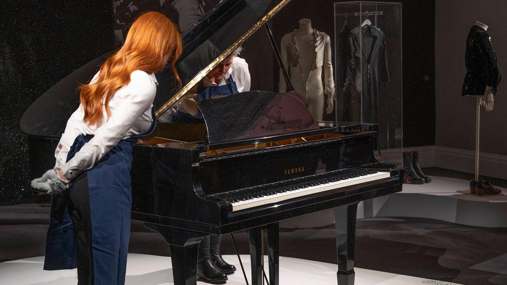 Man sieht das Yamaha G2 Baby Grand Piano. Eine Frau mit roten Haaren begutachtet das Piano. Man sieht das Yamaha G2 Baby Grand Piano. Eine Frau mit roten Haaren begutachtet das Piano.