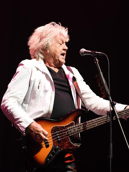 Der Musiker John Lodge steht in heller Jacke auf der Bühne und spielt seinen E-Bass