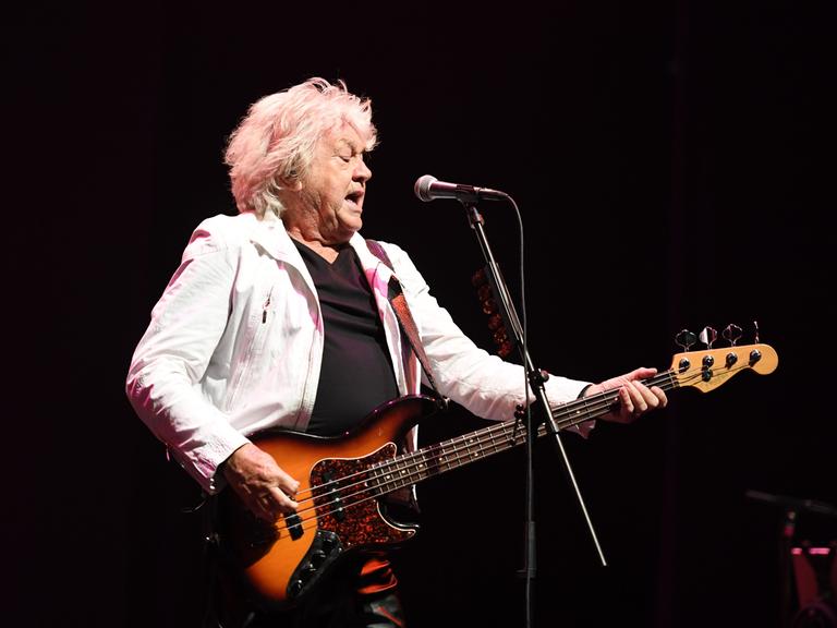 Der Musiker John Lodge steht in heller Jacke auf der Bühne und spielt seinen E-Bass
