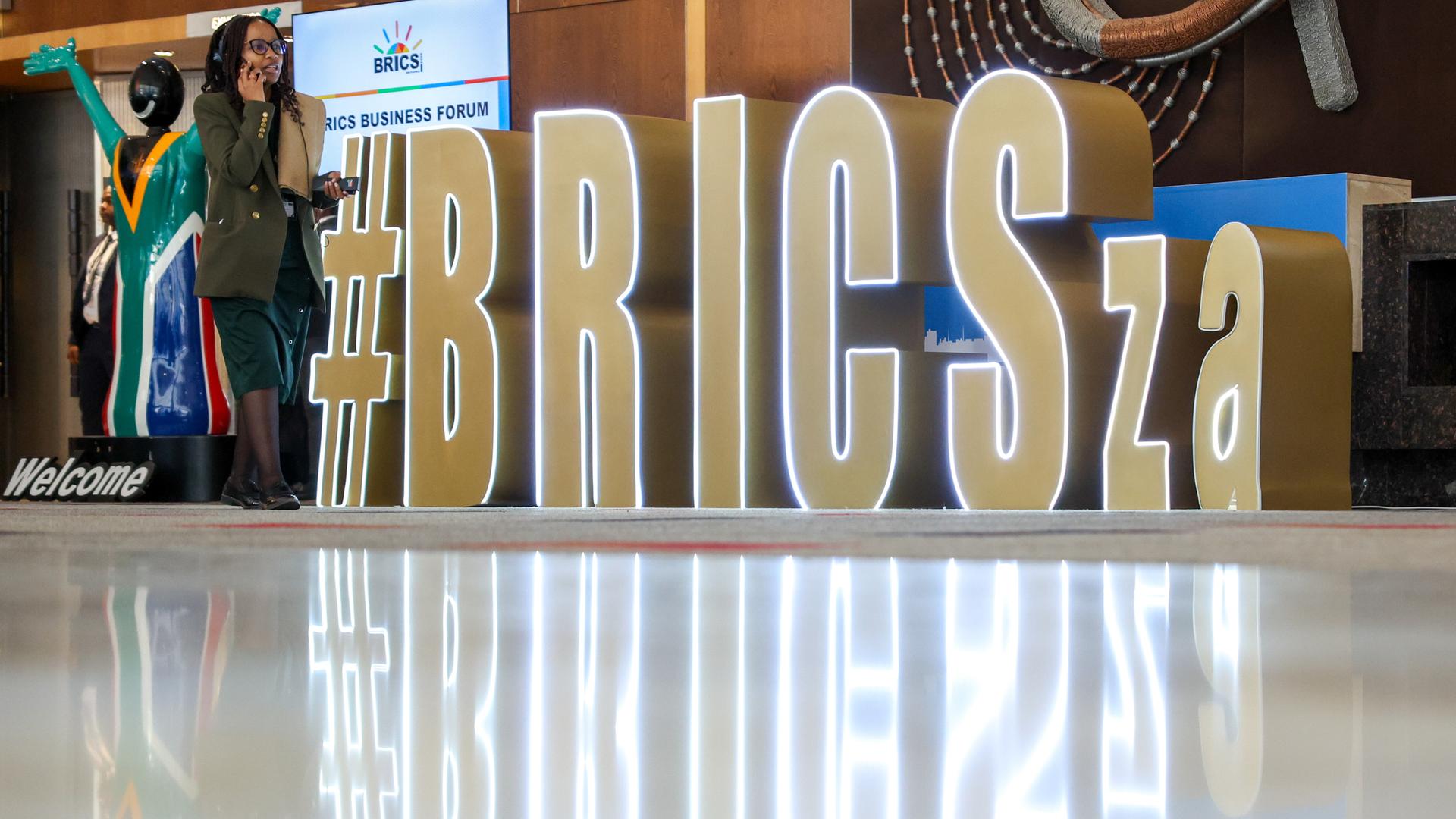 Am Rande des BRICS-Gipfels in Johannesburg sind die Buchstaben der Staatengruppen aufgestellt. Eine Frau läuft daran vorbei.