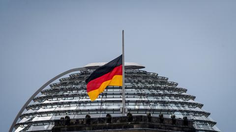 Eine der Deutschland-Flaggen auf dem Reichstag weht vor der Kulisse der Reichstagskuppel auf Halbmast. 