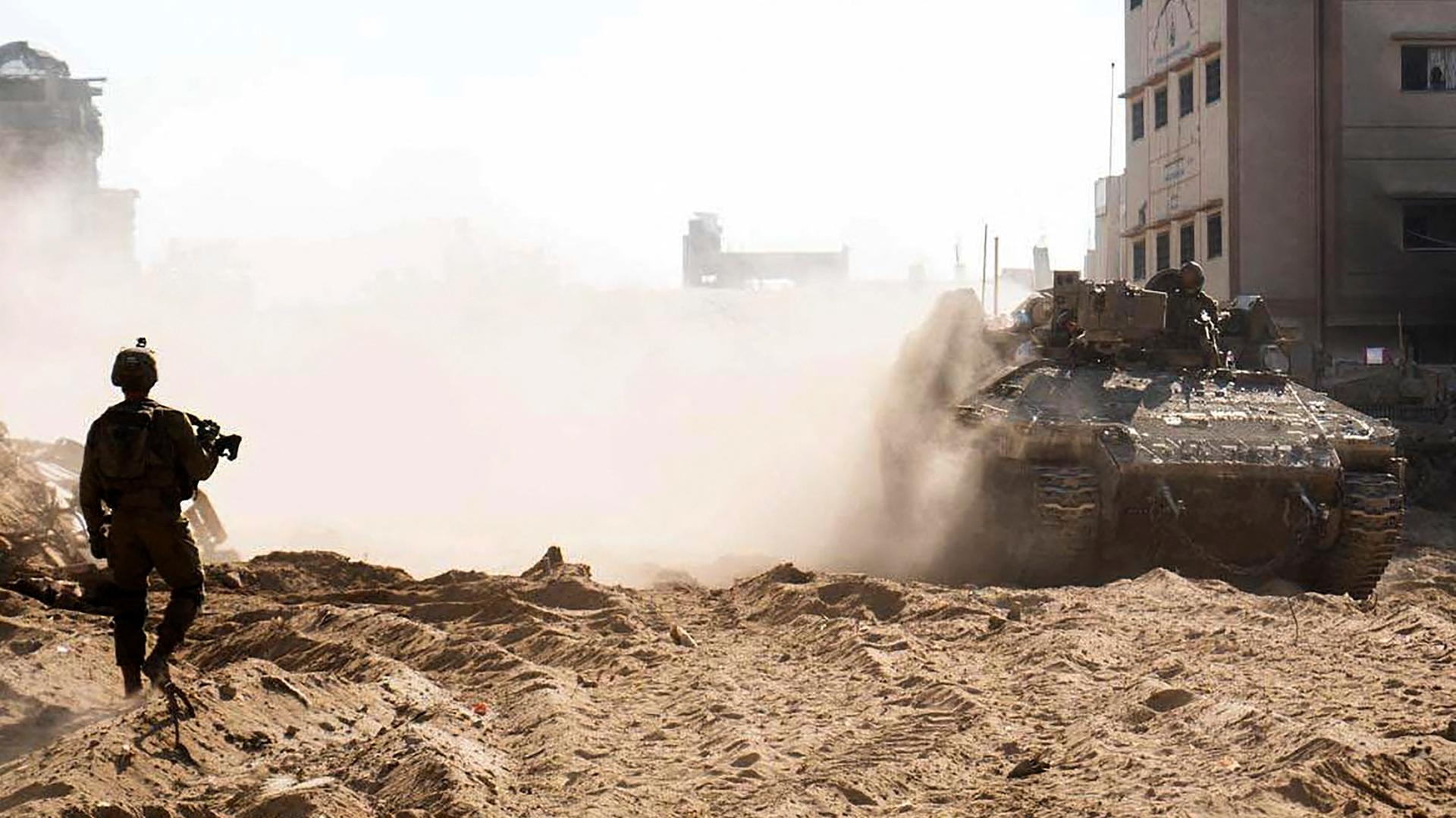 Euin israelischer Soldat läuft durch eine Trümmerlandschaft, über die dichter Rauch oder Staub zieht. Man sieht ihn als Silhouette von hinten.