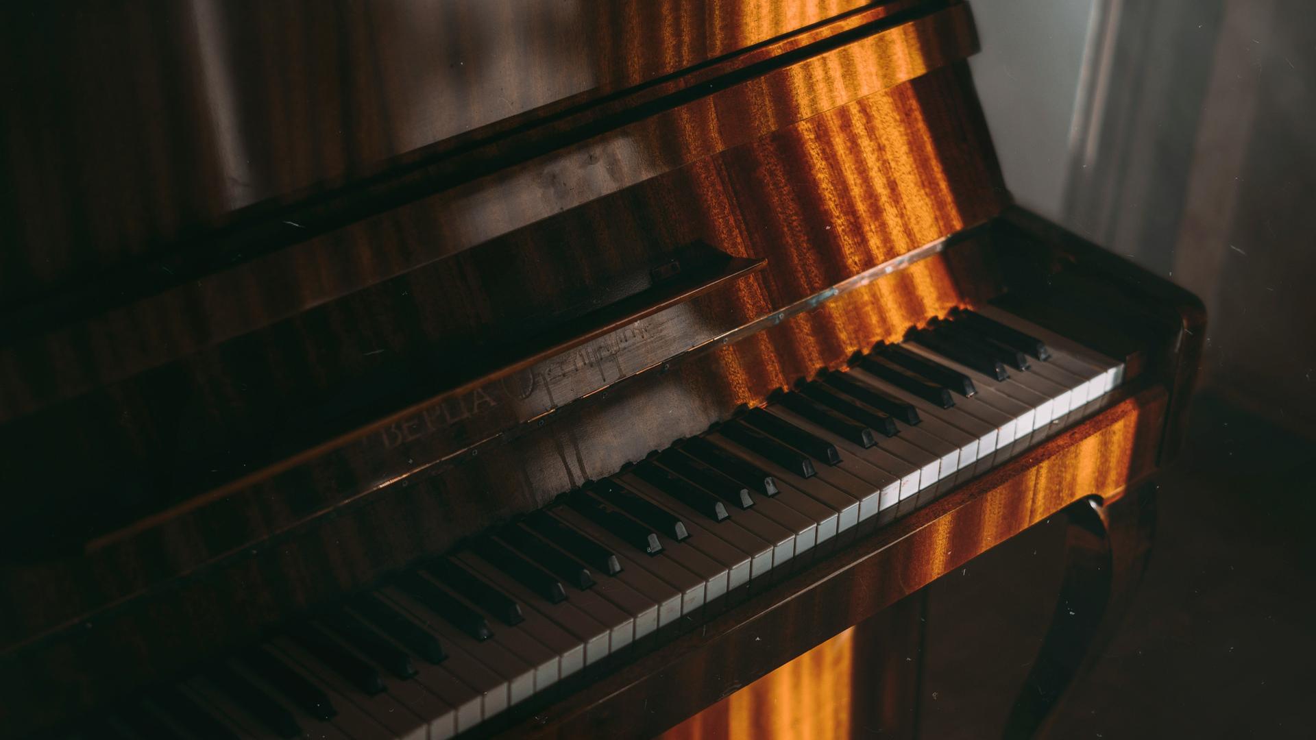 Blick auf hellbraun gemasertes Klavier, auf das markant Sonne durch ein Fenster fällt.