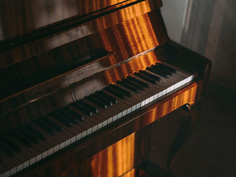 Blick auf hellbraun gemasertes Klavier, auf das markant Sonne durch ein Fenster fällt.