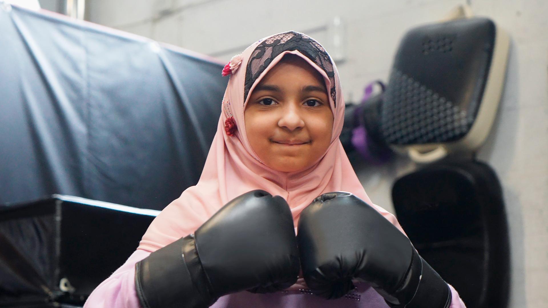 Ein Mädchen mit Hijan und Boxhandschuhen lächelt in die Kamera Ein Mädchen mit Hijan und Boxhandschuhen lächelt in die Kamera