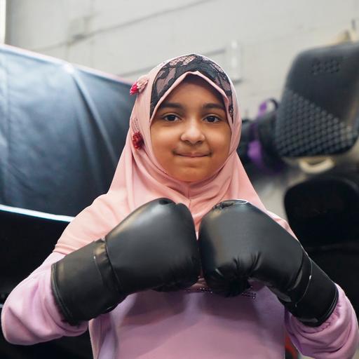 Ein Mädchen mit Hijan und Boxhandschuhen lächelt in die Kamera