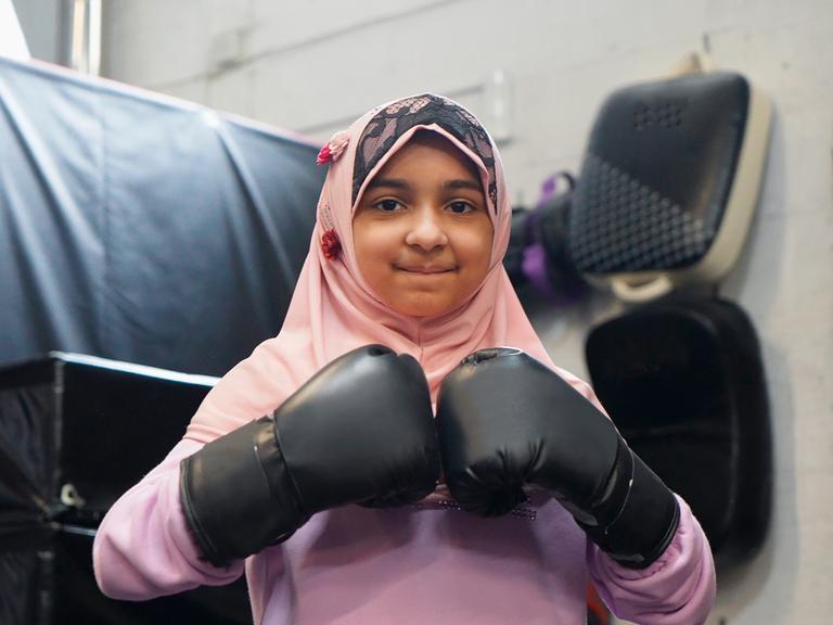 Ein Mädchen mit Hijan und Boxhandschuhen lächelt in die Kamera