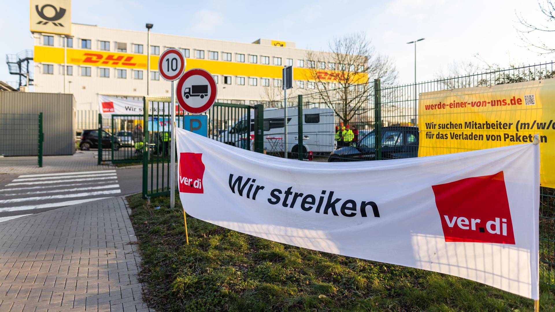 Ein Banner mit der Aufschrift "Wir streiken" der Gewerkschaft Ver.di hängt vor einem Gebäude des Paketdienstleisters DHL. Die Gewerkschaft Verdi hat Beschäftigte in allen Brief- und Paketzentren aufgerufen, die Arbeit niederzulegen.